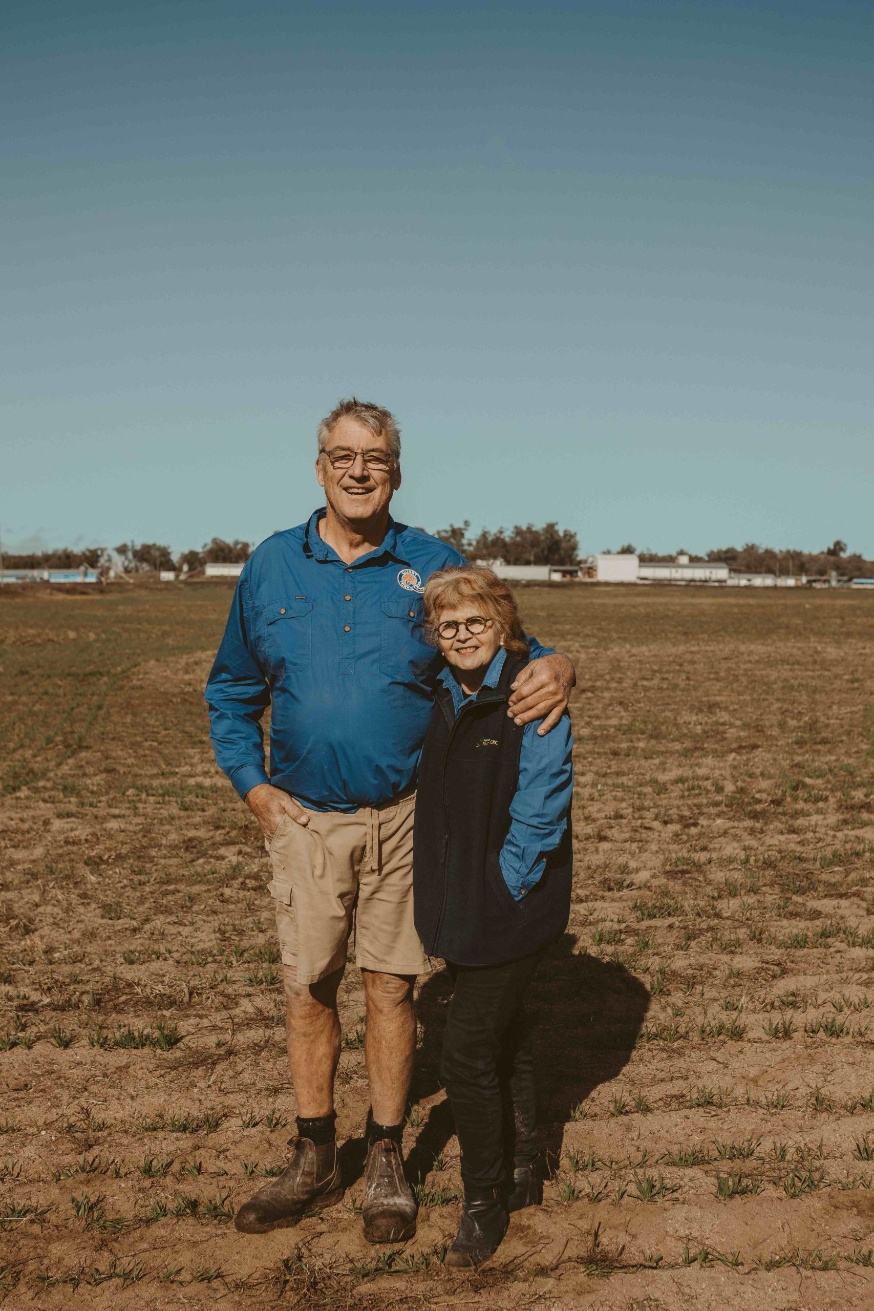 Husband and wife, Col and Vicki Quast, stand in front of sheds on their turkey farm