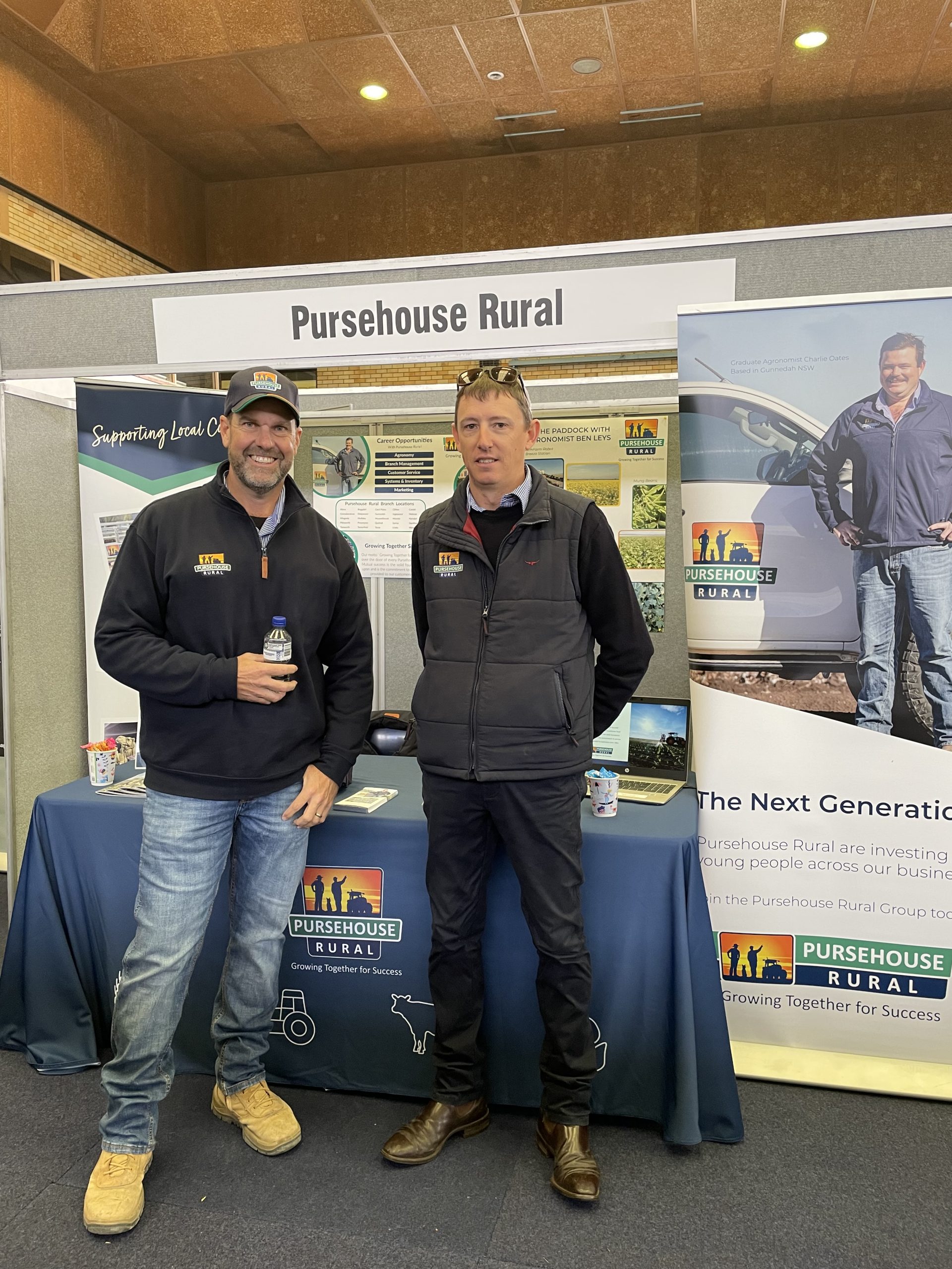 Two Pursehouse Rural employees stand in front of Pursehouse Rural branded booth at agriculture event